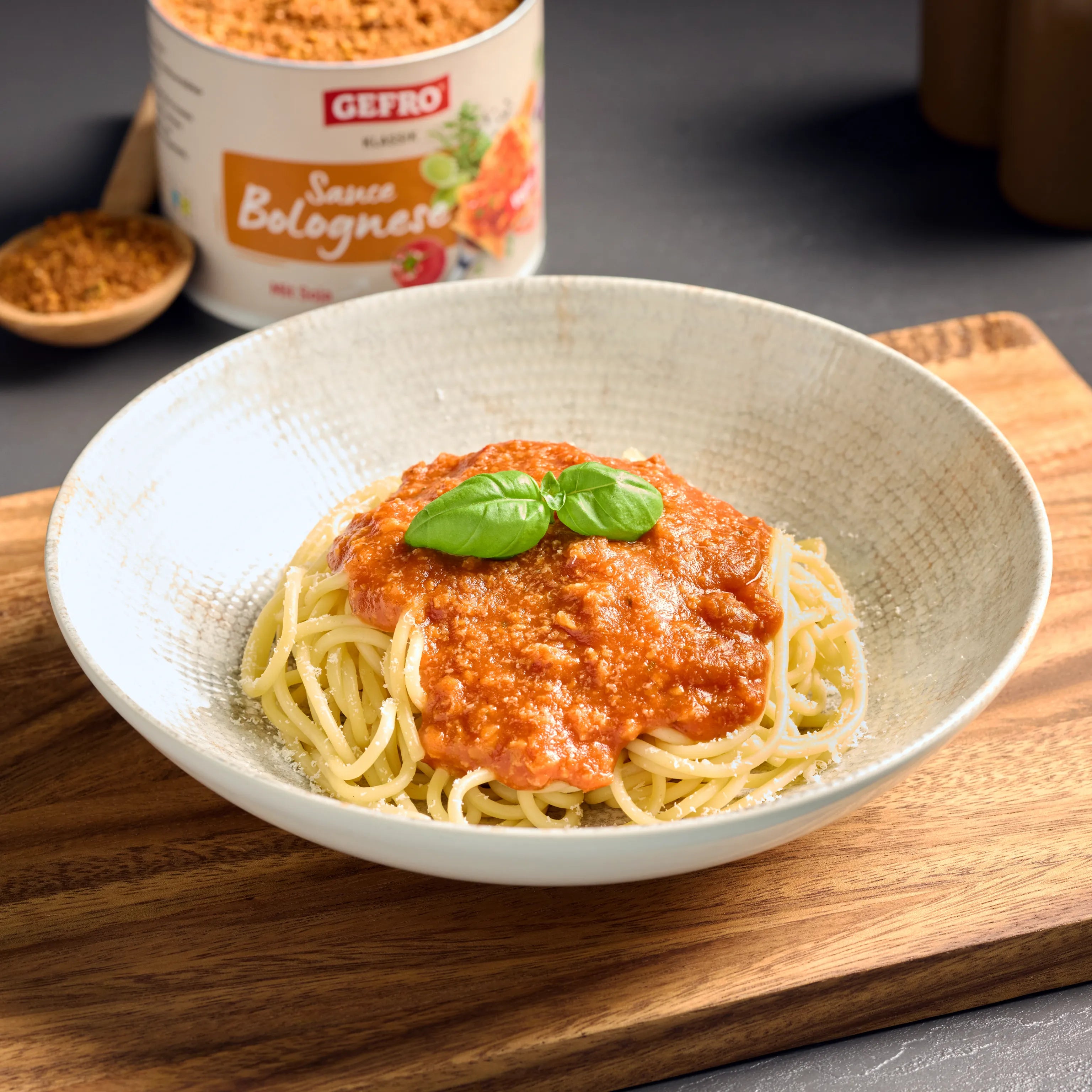 Teller mit Spaghetti und Bolognese-Sauce, garniert mit Basilikum; im Hintergrund steht eine Dose GEFRO Sauce Bolognese.