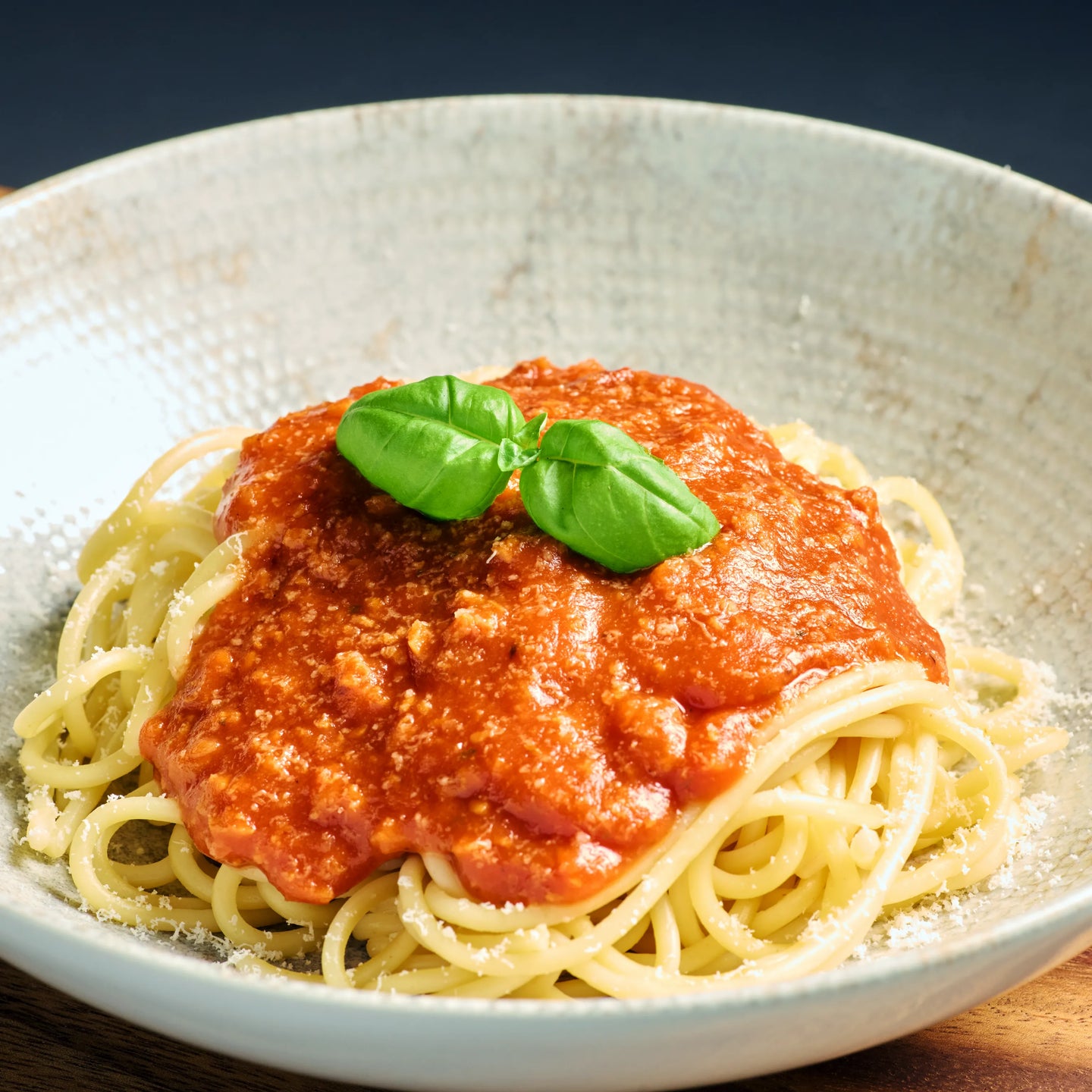 Teller mit Spaghetti in Tomatensoße, garniert mit frischem Basilikum und etwas geriebenem Käse am Rand