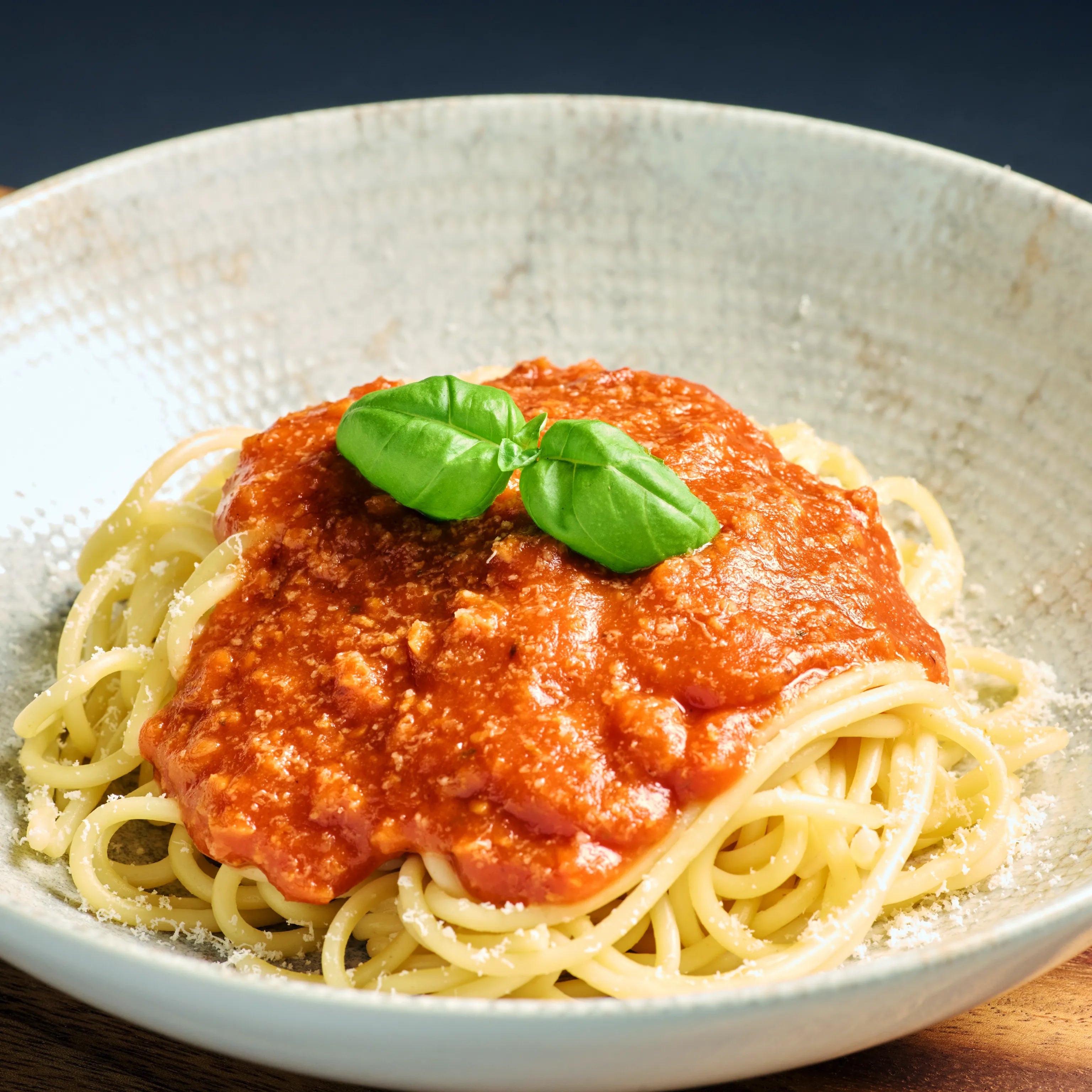 Teller mit Spaghetti in Tomatensoße, garniert mit frischem Basilikum und etwas geriebenem Käse am Rand