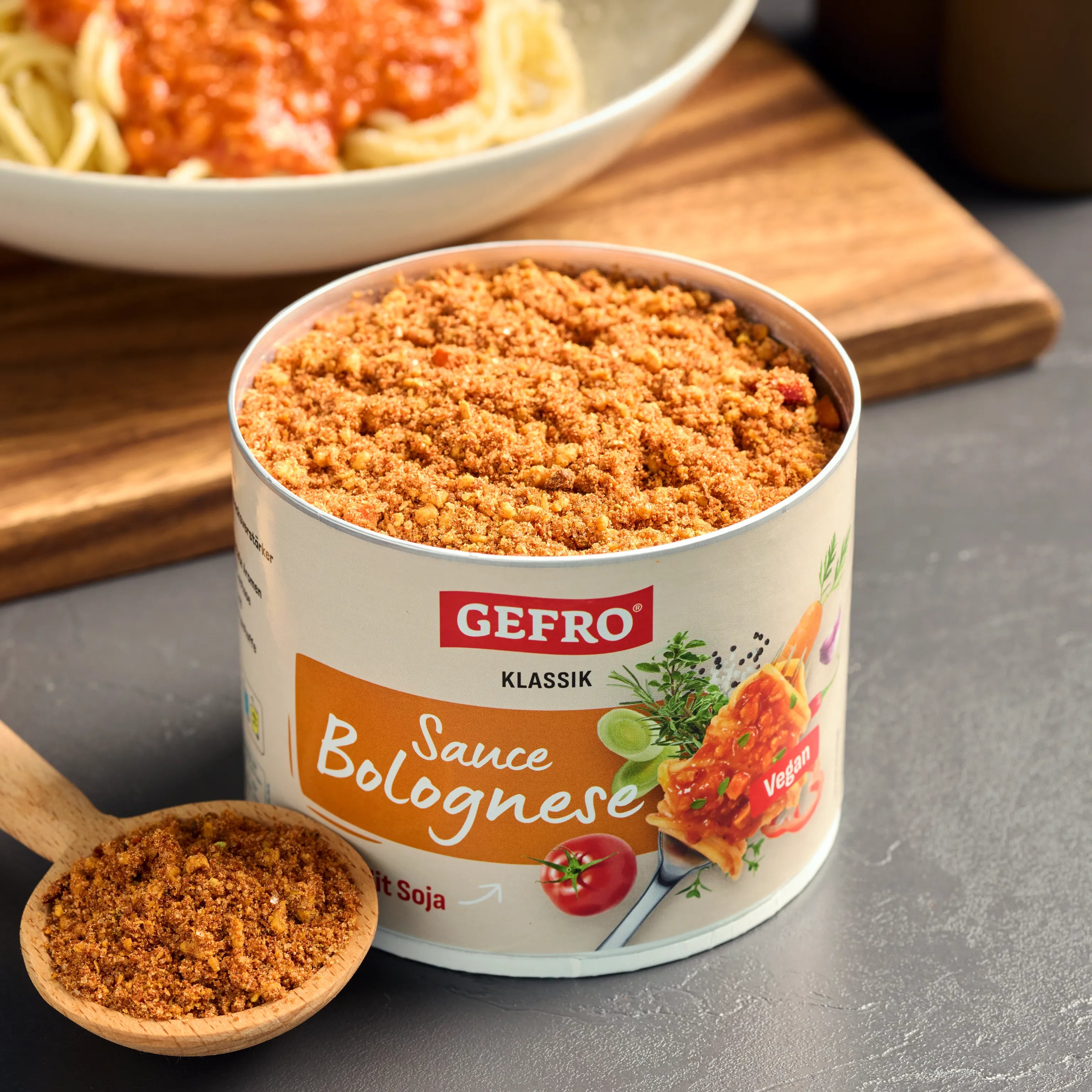 Offene Dose GEFRO Sauce Bolognese Klassik vegan mit Soja-Granulat und Holzlöffel, im Hintergrund ein Teller Pasta.