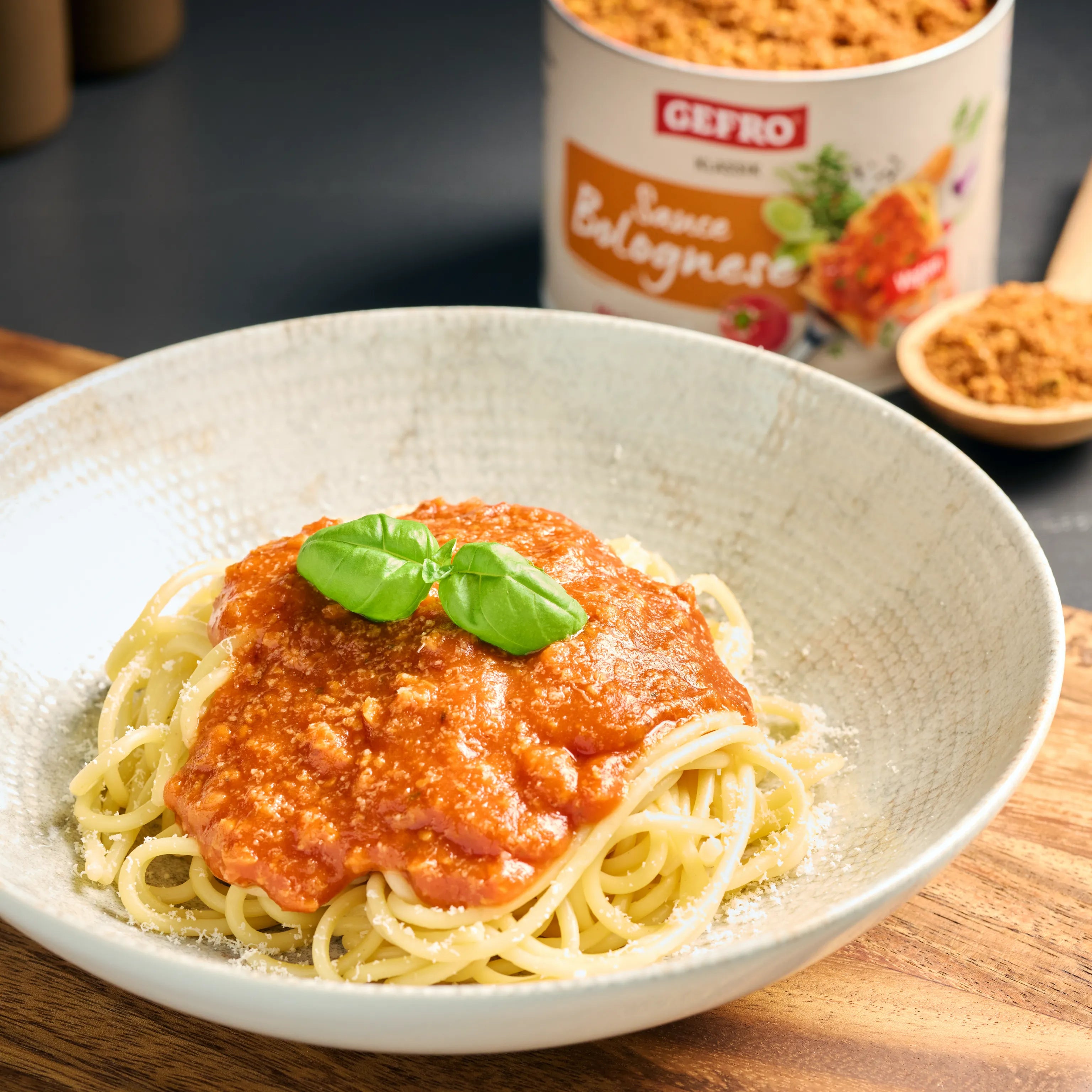 Teller mit Spaghetti und roter Bolognese-Sauce, garniert mit Basilikum; im Hintergrund ein passendes Gewürzprodukt.