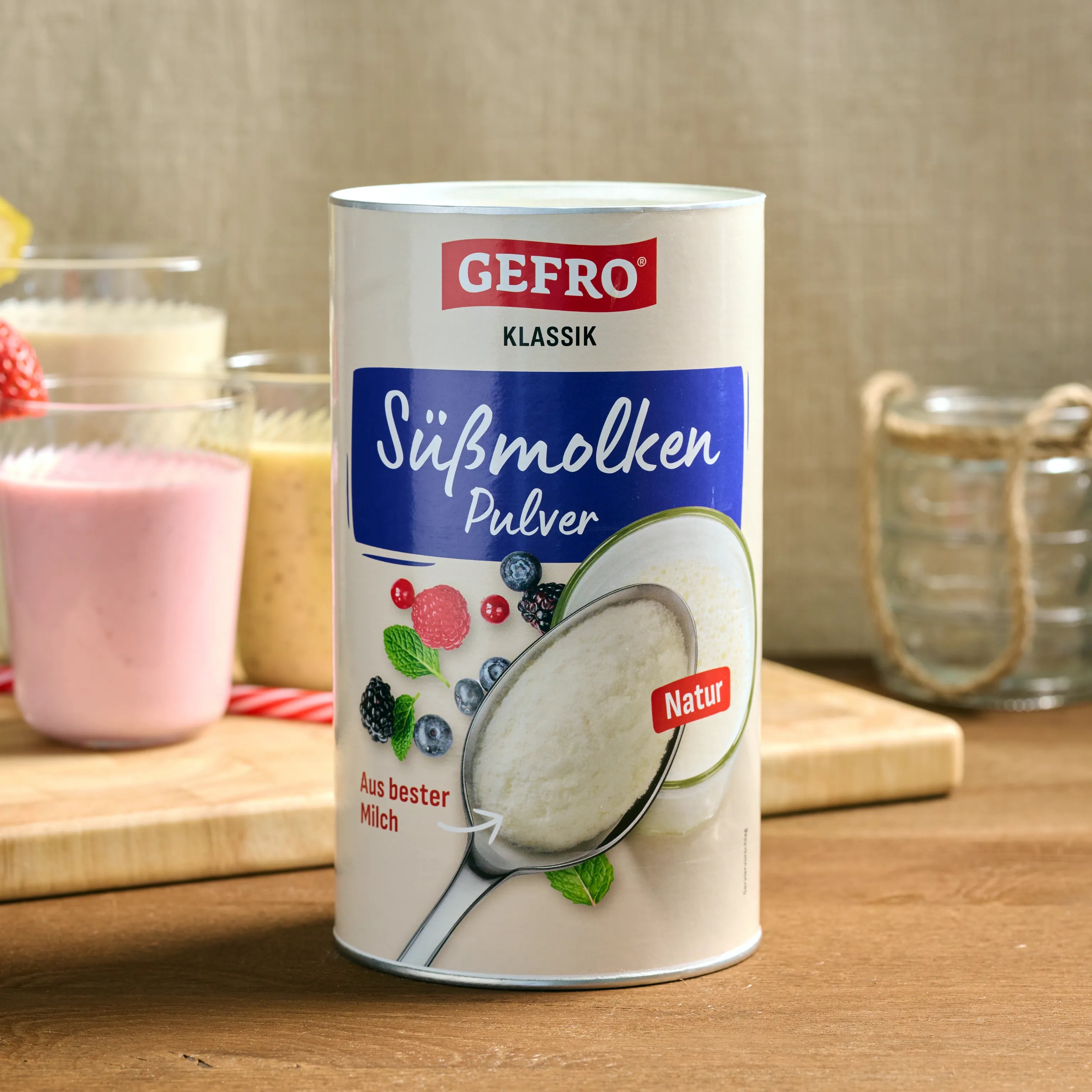Dose GEFRO Süßmolkenpulver Natur auf Holztisch, daneben Smoothies als Beispiel für die Verwendung in Getränken