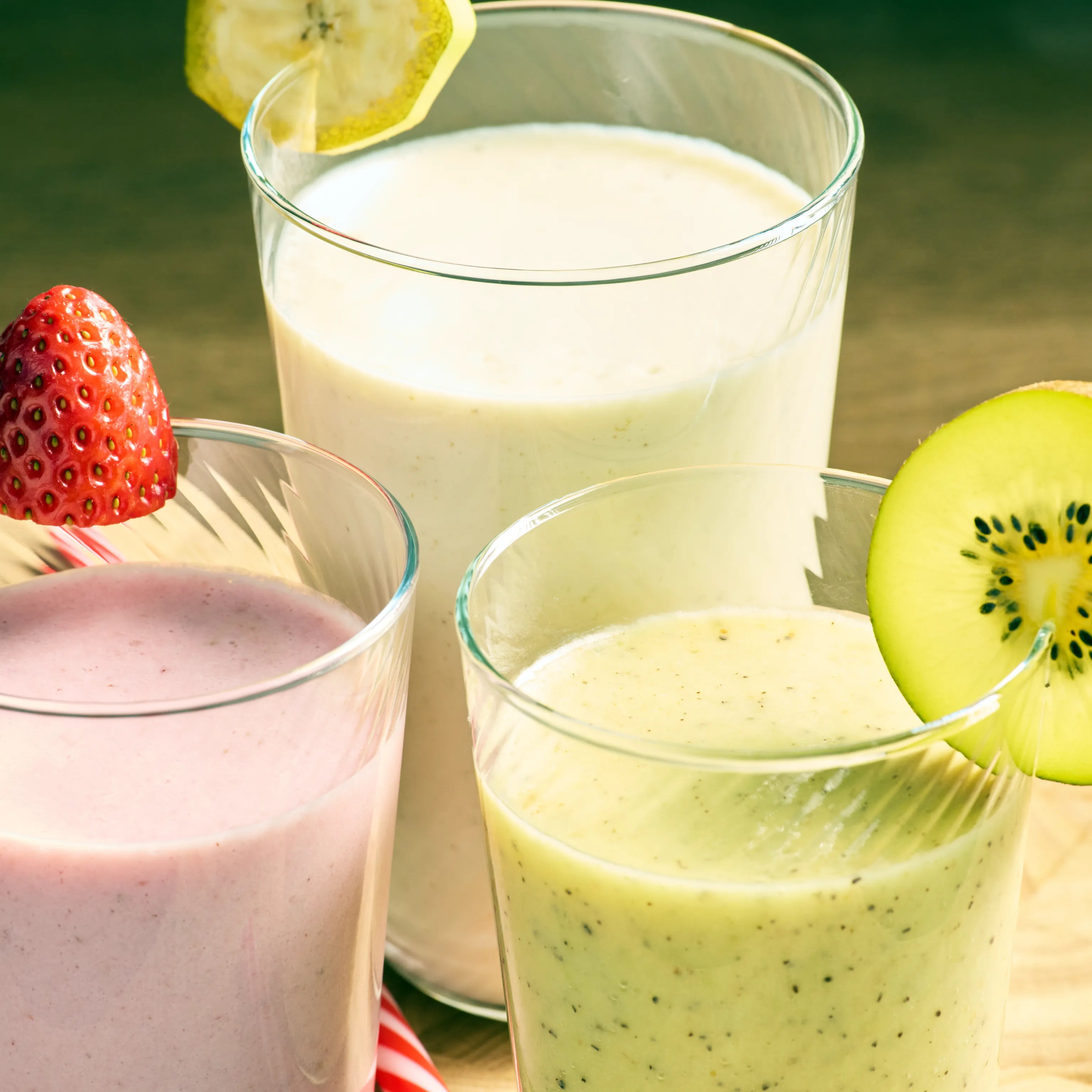 Drei Gläser mit Frucht-Smoothies in Rosa, Grün und Hellgelb, garniert mit Erdbeere, Kiwi und Zitronenscheibe.