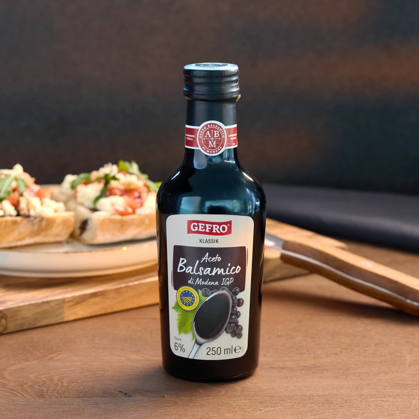 Flasche Gefro Aceto Balsamico di Modena IGP, 250 ml, auf Tisch vor Bruschetta als Produktbild in Küchenszene