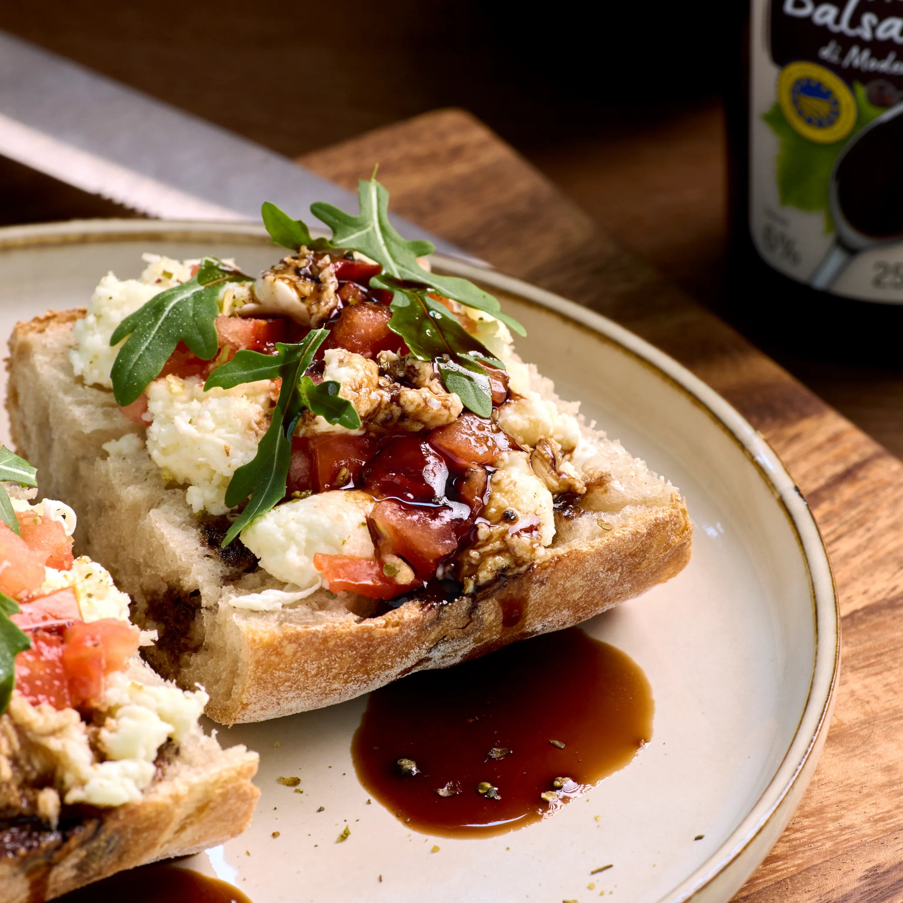 Belegtes Brot mit Tomaten, weichem Käse, Rucola und Balsamico-Creme auf einem Teller aus Keramik