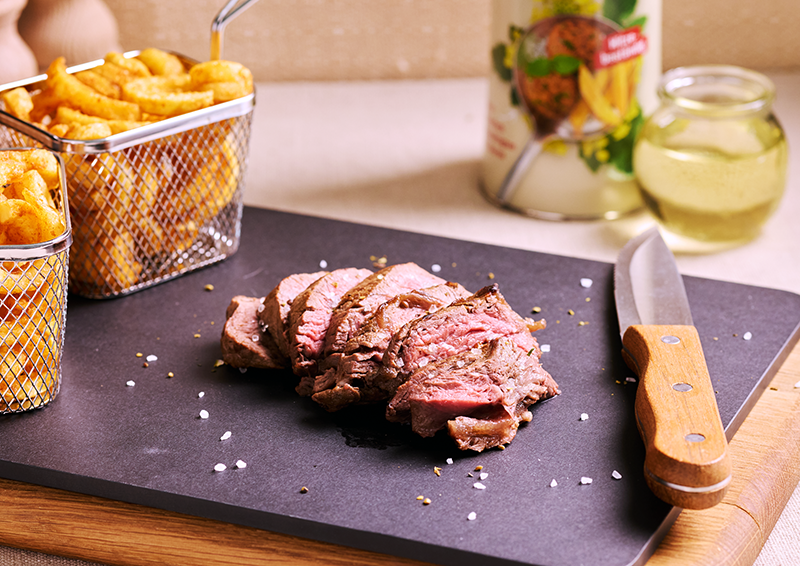 Geschnittenes Roastbeef auf schwarzer Platte mit Pommes im Korb und Messer, servierfertig angerichtet