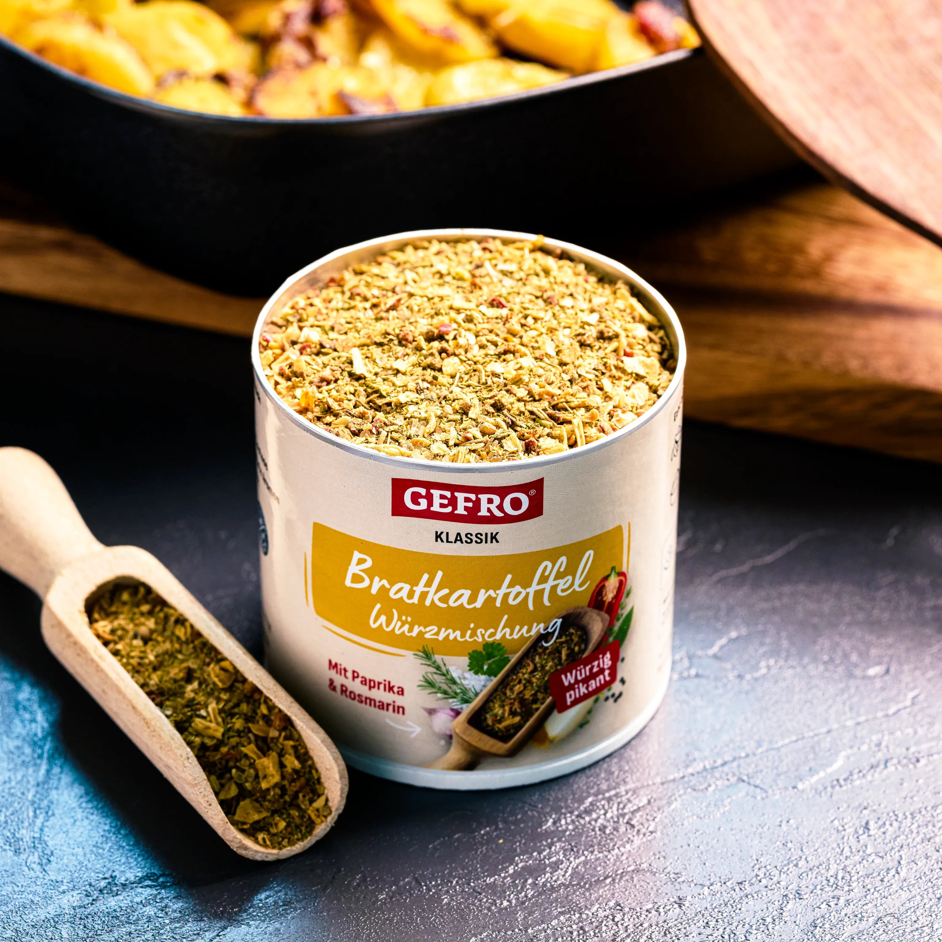 Offene Dose GEFRO Bratkartoffel Würzmischung mit Holzschaufel, im Hintergrund eine Pfanne mit Bratkartoffeln
