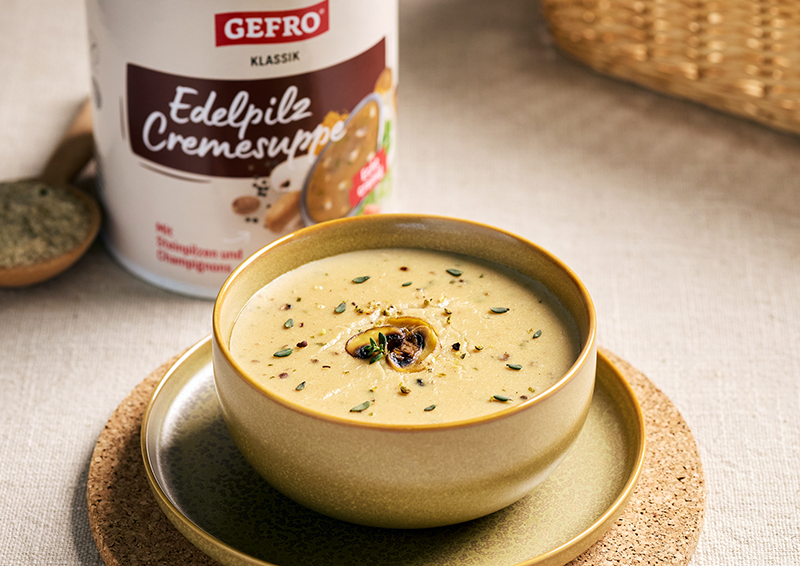 Schale mit cremiger Edelpilz-Cremesuppe, garniert mit Pilz und Kräutern, daneben GEFRO Klassik Verpackung