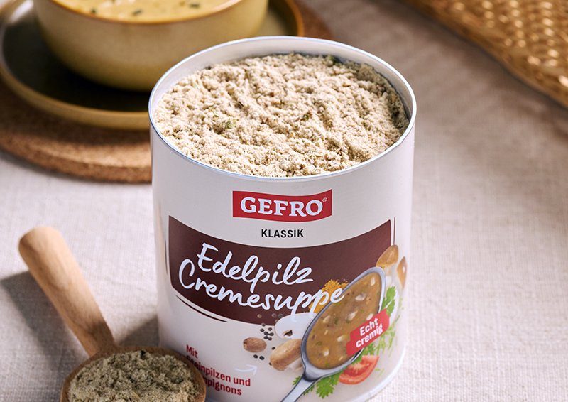 Offene Dose GEFRO Edelpilz Cremesuppe mit Suppenpulver auf Tisch, daneben Holzlöffel und Schale im Hintergrund
