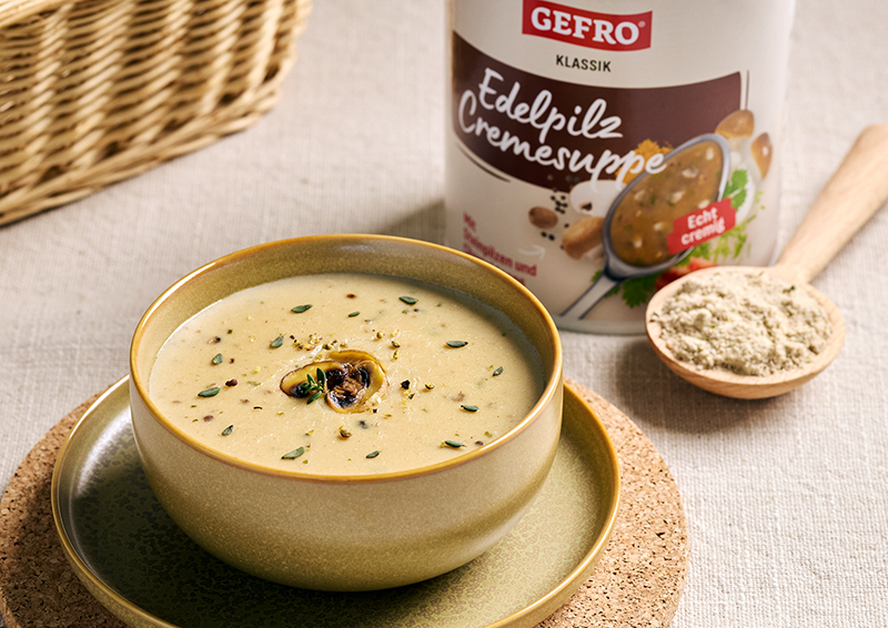 Cremige Edelpilz-Cremesuppe in einer Schale, garniert mit Pilzen und Kräutern, daneben GEFRO Klassik Dose und Pulverlöffel
