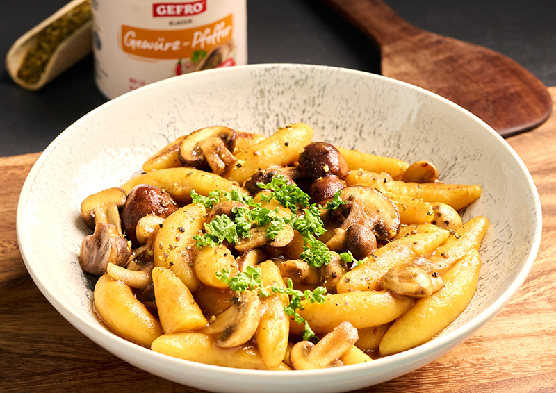 Schupfnudeln mit gebratenen Champignons und Petersilie in einer Schale, appetitlich angerichtet auf Holzbrett