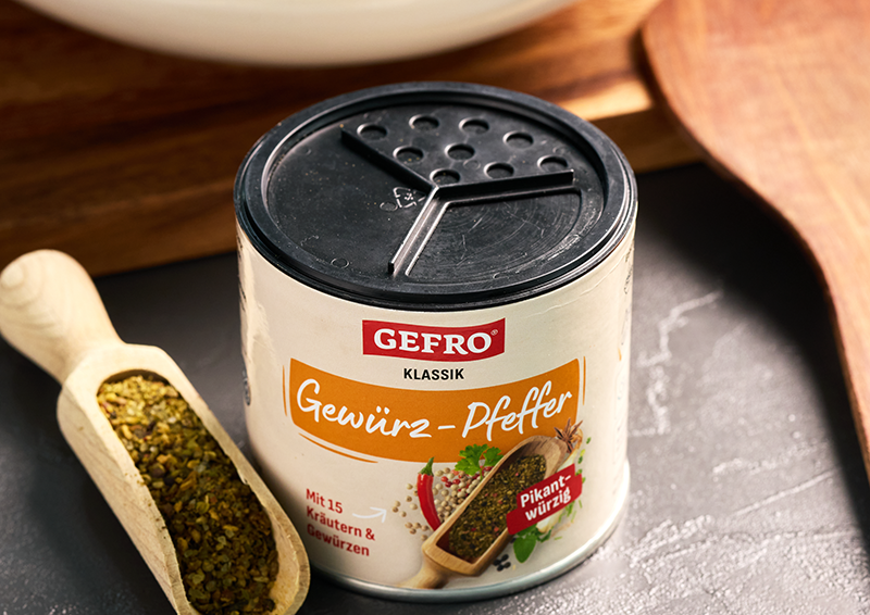 Dose GEFRO Klassik Gewürz-Pfeffer mit schwarzem Deckel neben Holzschaufel mit Gewürzmischung auf dunkler Fläche