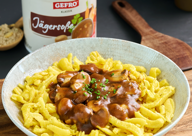 Spätzle mit brauner Pilzsoße und Schnittlauch in einer Schale, daneben im Hintergrund eine Dose Jägersuppe
