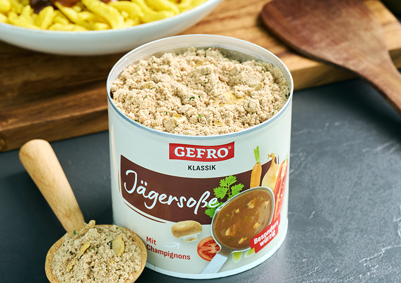 Dose GEFRO Jägersoße Klassik mit Pulver auf Küchenfläche, daneben Holzlöffel und Schüssel mit Nudeln