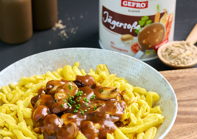 Spätzle mit brauner Jägersoße und Champignons auf einem Teller, dahinter eine Dose Gefro Jägersoße Klassik