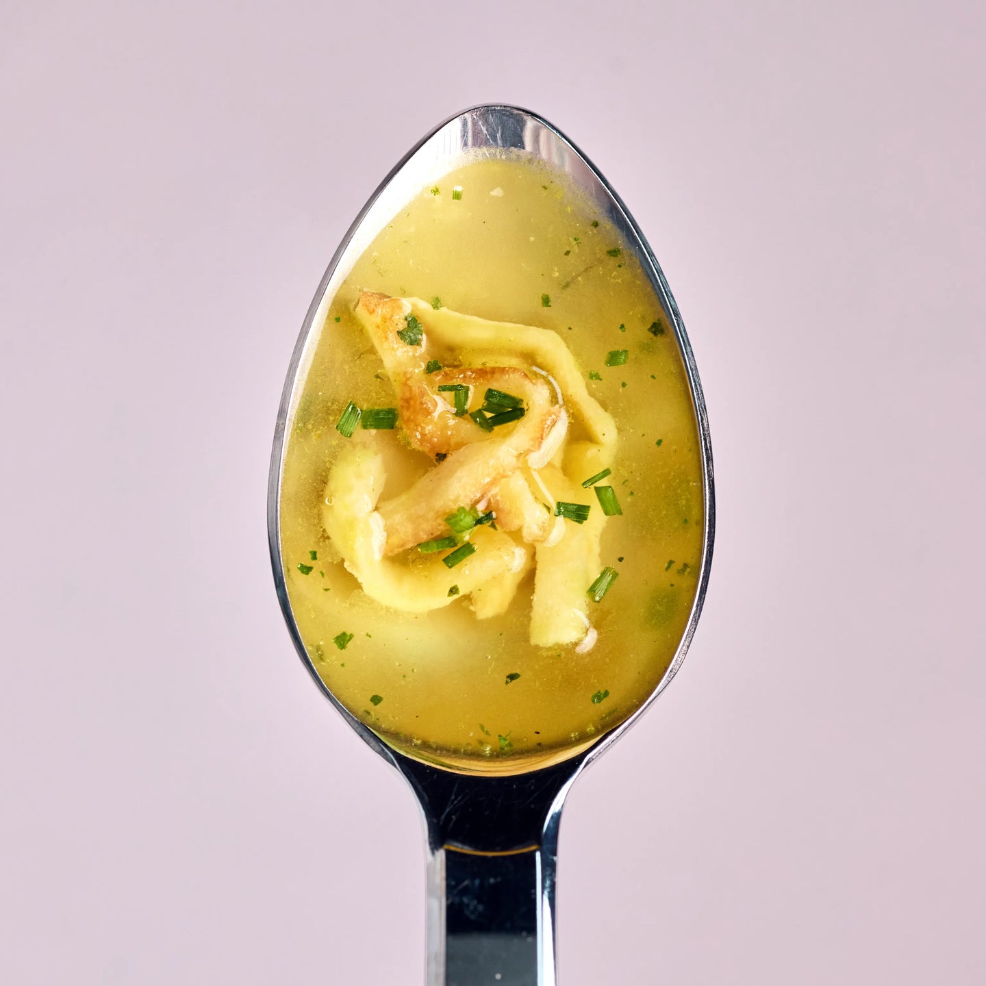 Löffel mit klarer Brühe, gefüllten Teigtaschen und frischen Kräutern als appetitliche Nahaufnahme