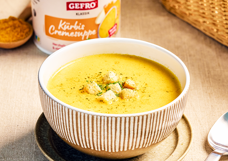 Schüssel mit cremiger Kürbissuppe und Croûtons auf Untertasse, im Hintergrund eine Dose Gefro Kürbis Cremesuppe