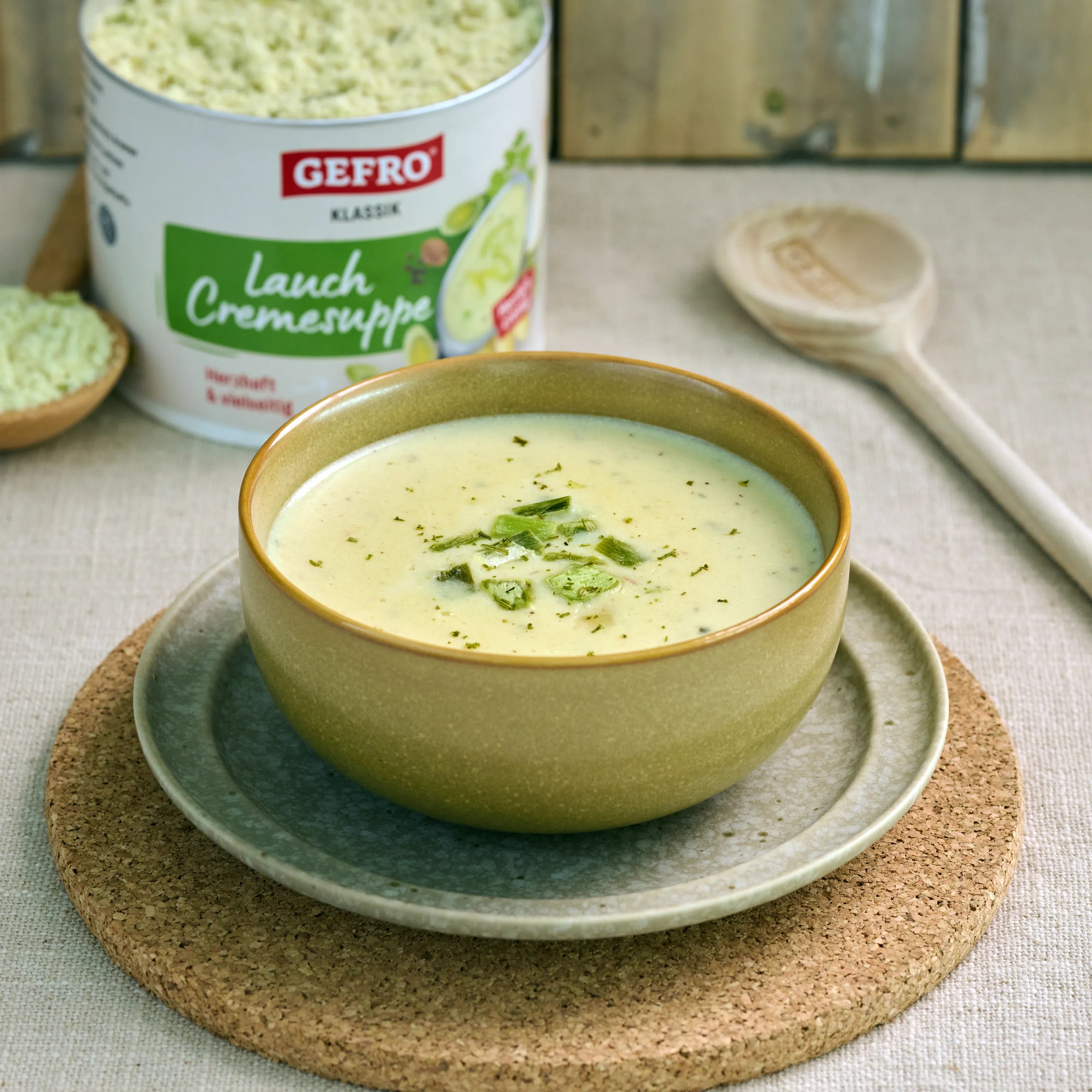 Schale mit cremiger Lauchsuppe auf Teller, dahinter geöffnete Dose GEFRO Lauch Cremesuppe auf dem Tisch