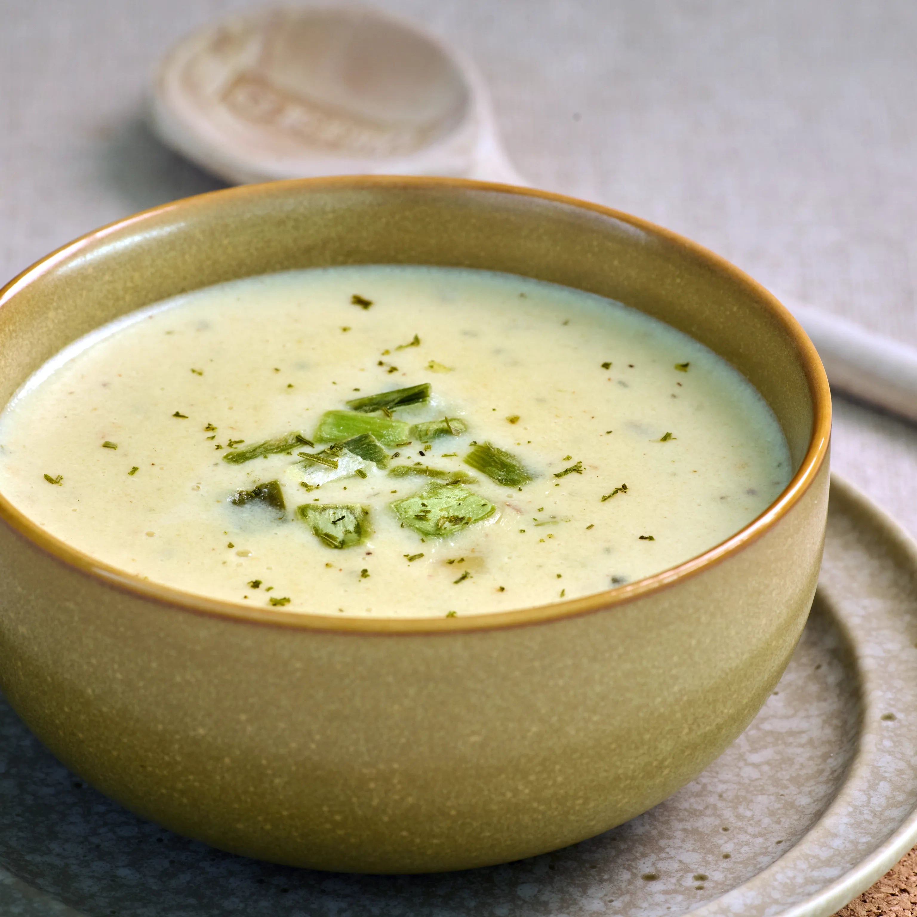 Schale mit cremiger, heller Suppe, garniert mit Frühlingszwiebeln, auf einem Teller serviert auf hellem Tisch.