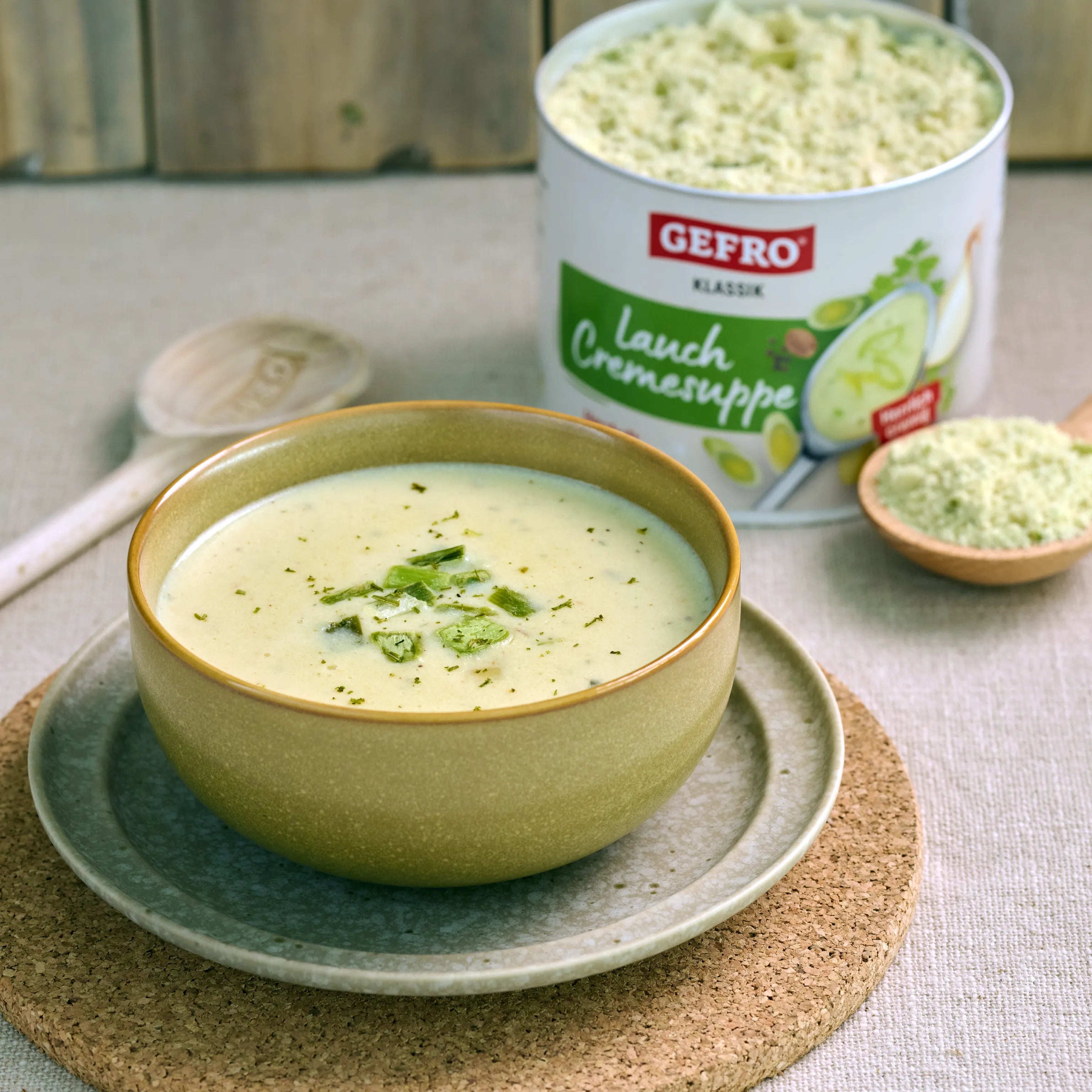 Schüssel mit heller Lauch-Cremesuppe auf Teller, daneben Dose und Pulver der Gefro Klassik Lauch Cremesuppe