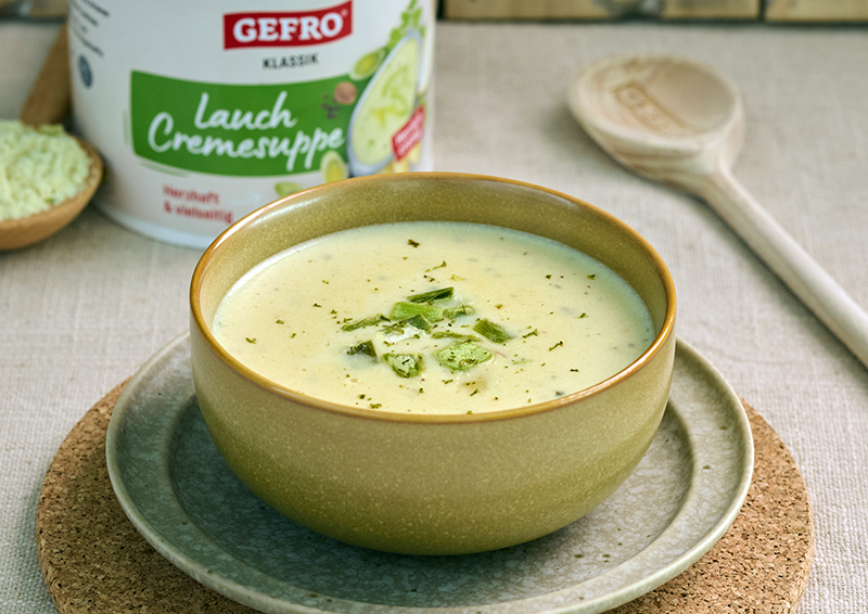 Schale mit cremiger Lauch-Cremesuppe auf Teller, im Hintergrund GEFRO Klassik Dose und Holzlöffel