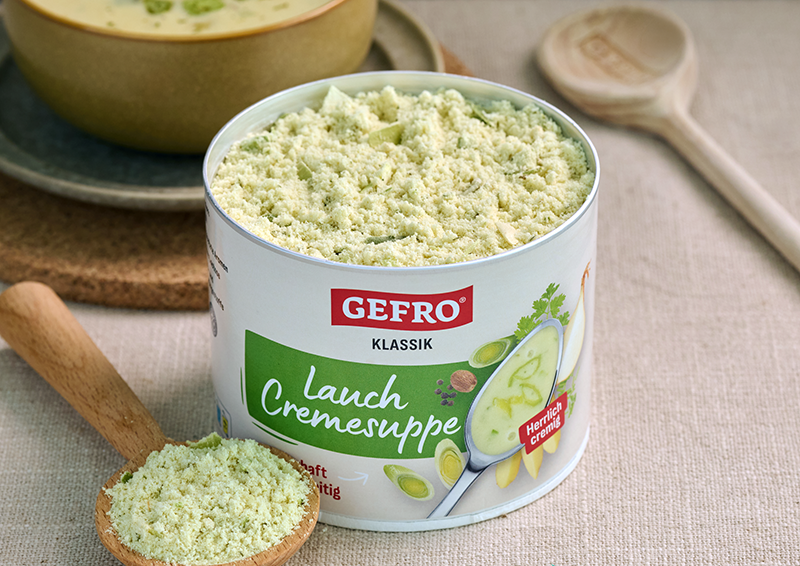Dose GEFRO Lauch Cremesuppe mit geöffnetem Suppenpulver und Holzlöffel auf Tisch, geeignet für cremige Lauchsuppe