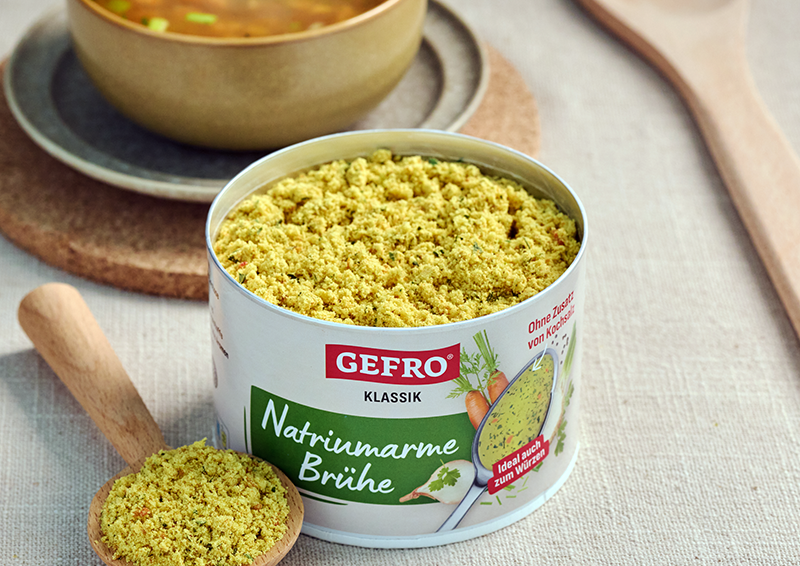 Dose GEfro natriumarme Brühe mit geöffnetem Inhalt und Holzlöffel auf Tisch, geeignet zum Würzen und Kochen