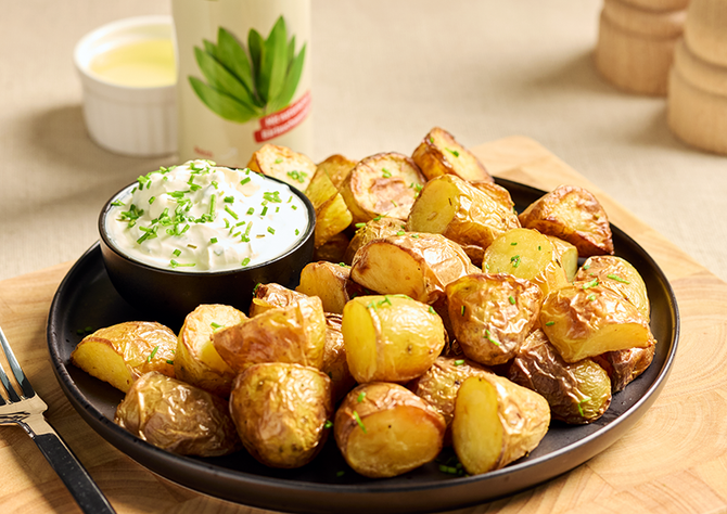 Schale mit knusprigen Ofenkartoffeln und cremigem Dip mit Schnittlauch auf einem Holzbrett serviert