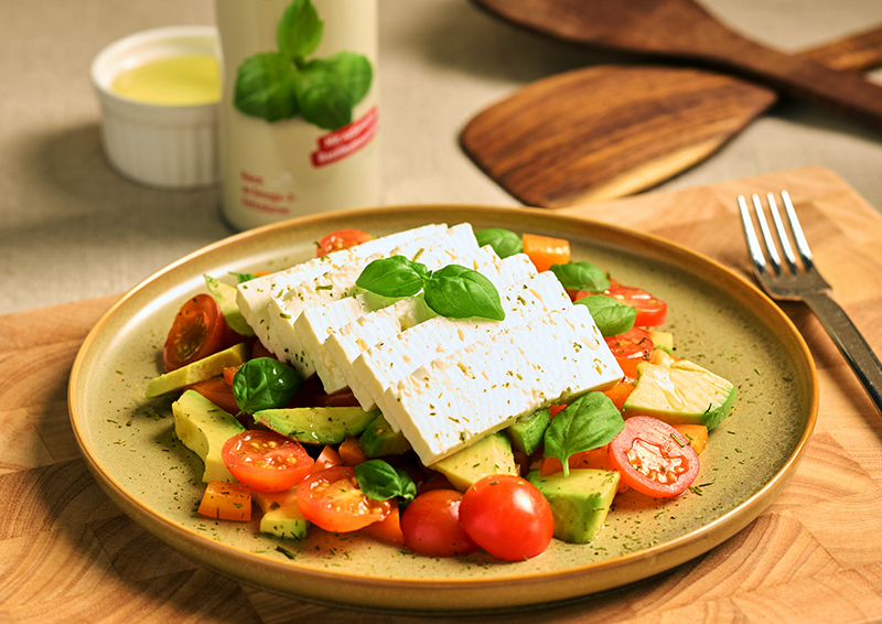 Salat mit Feta, Avocado, Cherrytomaten und Basilikum auf einem Teller, dekorativ angerichtet auf Holztisch