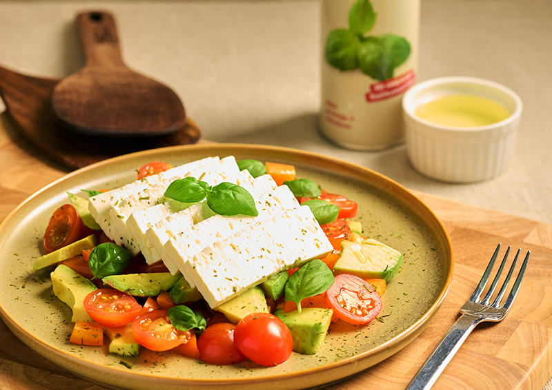 Salat mit Feta, Avocado, Tomaten und Basilikum auf Teller, dekorativ angerichtet auf Holzunterlage