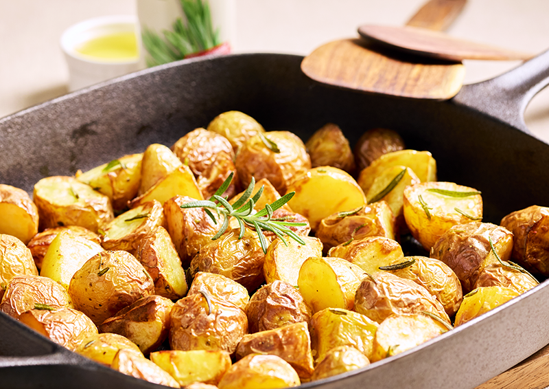 Geröstete Kartoffelstücke mit Rosmarin in einer Pfanne, goldbraun gebacken als Beilage oder Ofengericht
