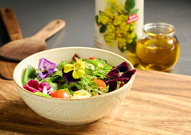 Schüssel mit frischem gemischtem Salat, essbaren Blüten und Dressing auf Holztisch angerichtet