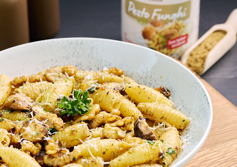 Schale mit Pasta in Pilz-Pesto, garniert mit Parmesan und Petersilie, daneben Pesto-Glas im Hintergrund