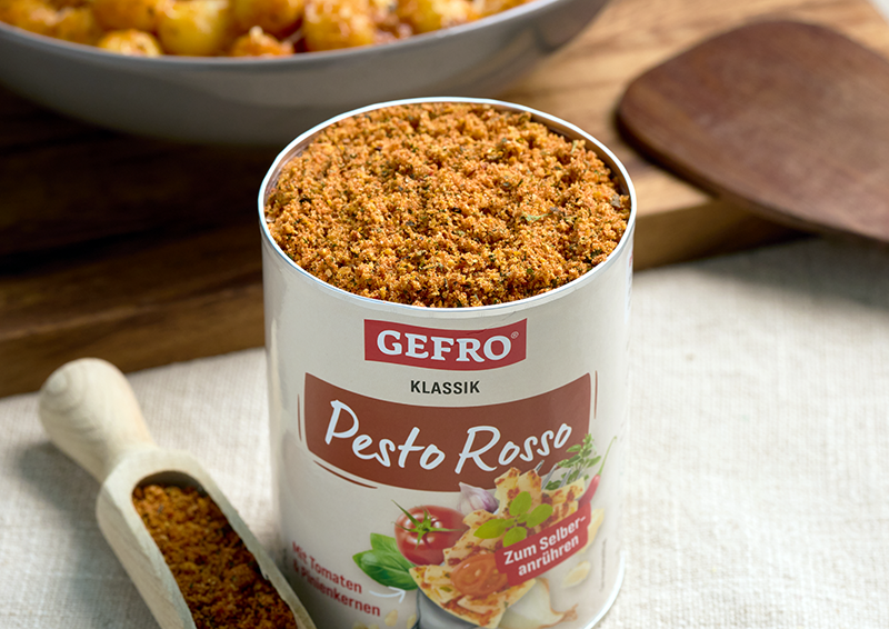Dose GEFRO Klassik Pesto Rosso mit offenem Inhalt auf Tisch, daneben Holzschaufel mit Gewürzmischung