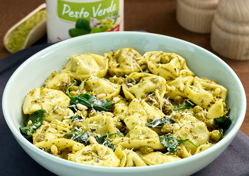 Schüssel mit Tortellini in grünem Pesto, mit Spinat, Erbsen, Pinienkernen und geriebenem Käse serviert
