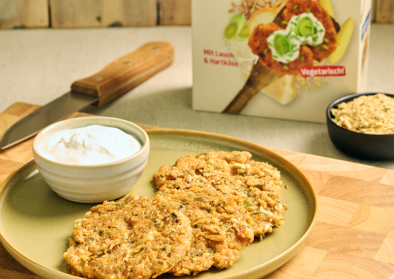 Vegetarische Bratlinge auf grünem Teller mit Dip in Schale, daneben Verpackung und Schüssel mit Paniermehl