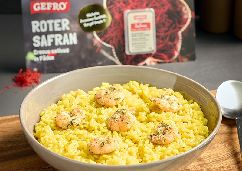 Schale mit gelbem Safranreis und Garnelen, dahinter Verpackung von GEFRO Roter Safran zum Würzen und Kochen