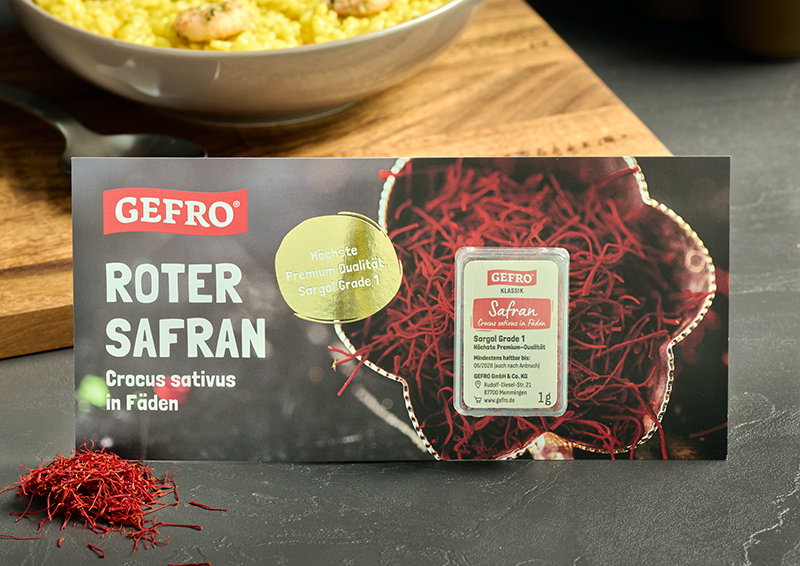 Verpackung und Dose mit rotem Safran in Fäden von Gefro, dekorativ vor einer Schale mit gelbem Reis platziert
