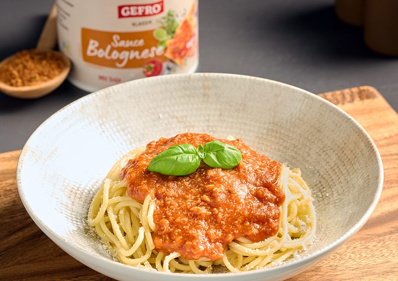 Teller mit Spaghetti und Bolognese-Sauce, garniert mit Basilikum; im Hintergrund steht eine Dose der Sauce.