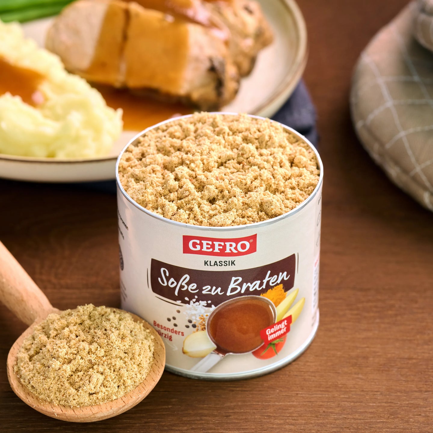 Dose GEFRO Soße zu Braten Klassik mit Pulver auf Holztisch, daneben Löffel und Teller mit Braten und Kartoffelpüree