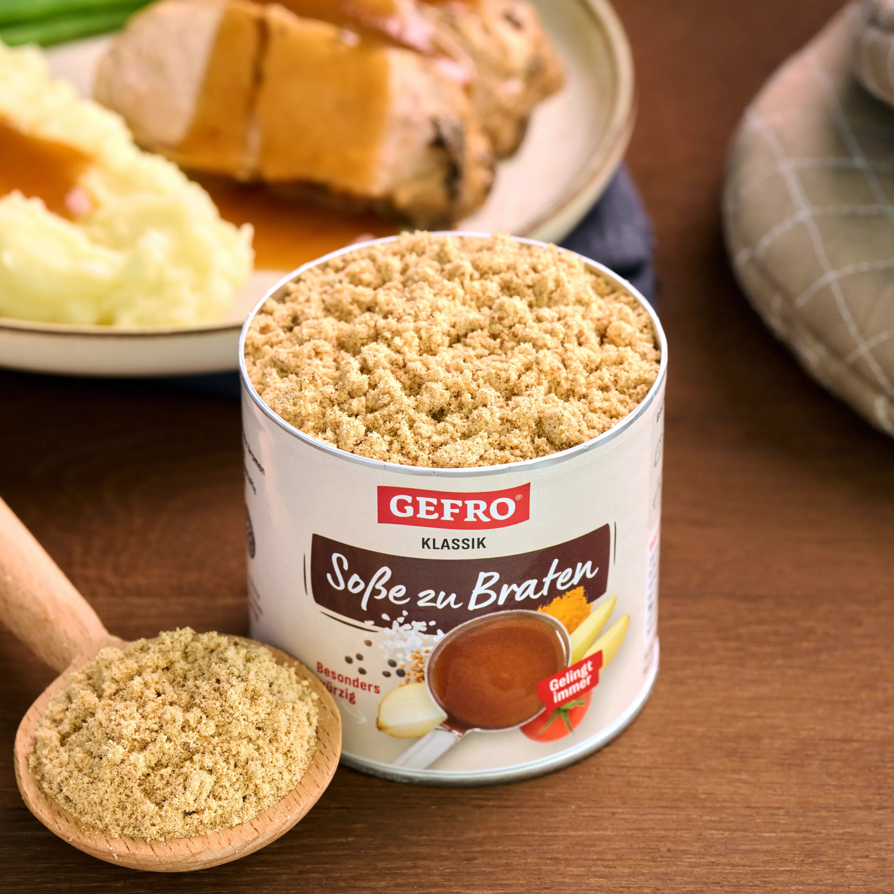 Dose GEFRO Soße zu Braten Klassik mit Pulver auf Holztisch, daneben Löffel und Teller mit Braten und Kartoffelpüree