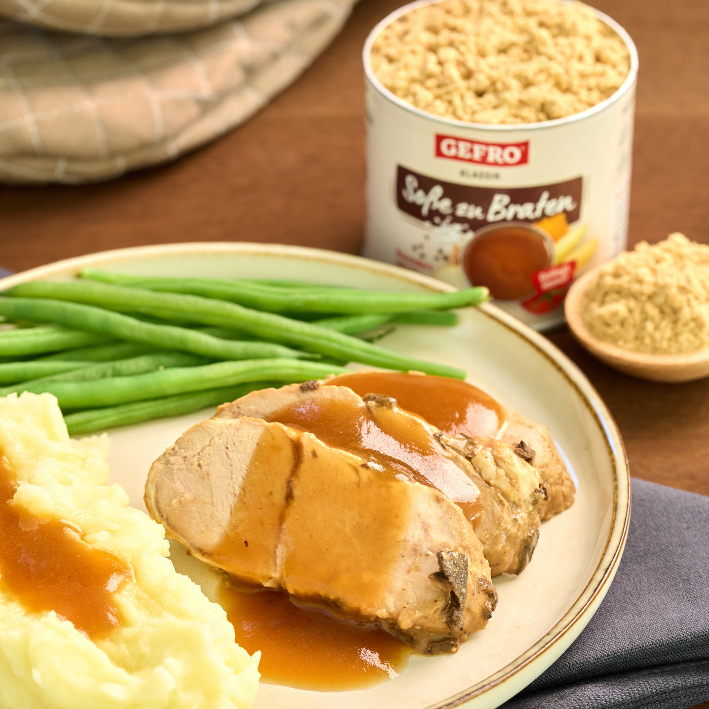 Teller mit Braten, Kartoffelpüree und grünen Bohnen, daneben Dose und Pulver für Soße zum Braten.