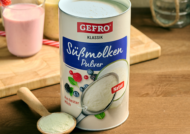 Dose GEFRO Süßmolkenpulver Natur auf Holztisch, daneben ein Löffel mit Pulver zur Dosierung