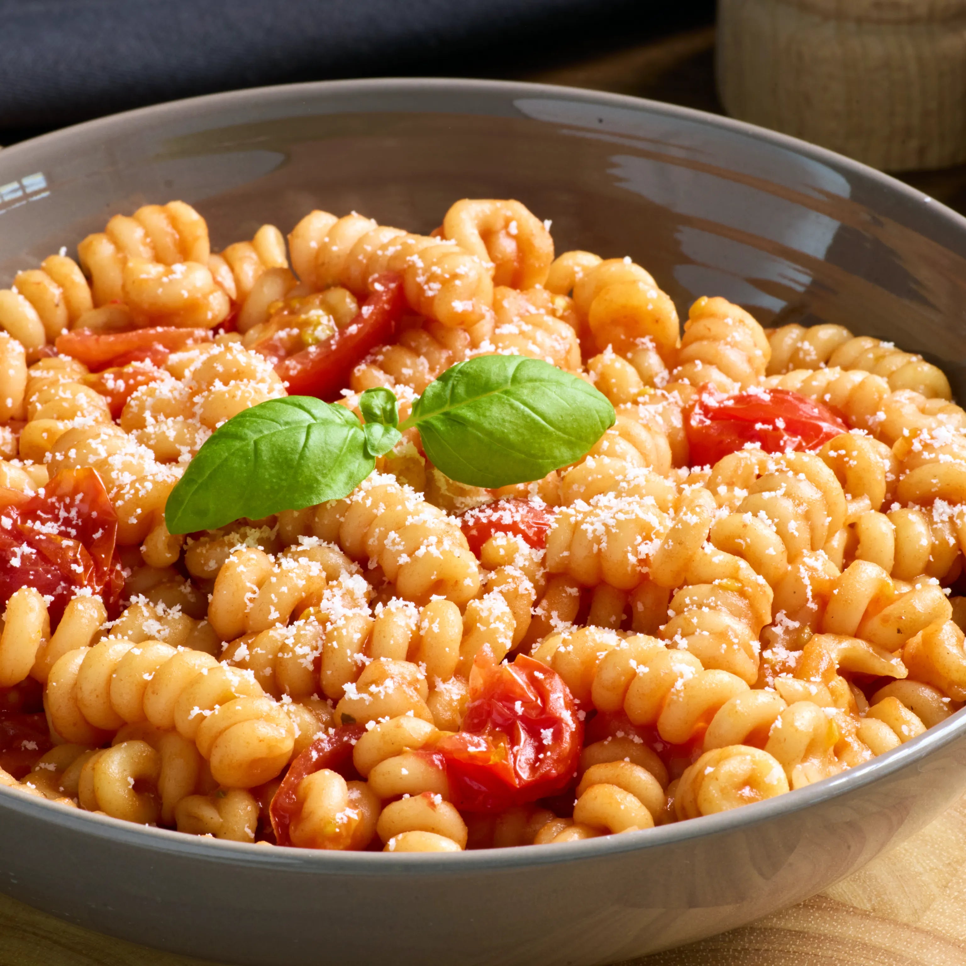 Schüssel mit Fusilli in Tomatensauce, Kirschtomaten, geriebenem Käse und Basilikum als serviertes Pastagericht