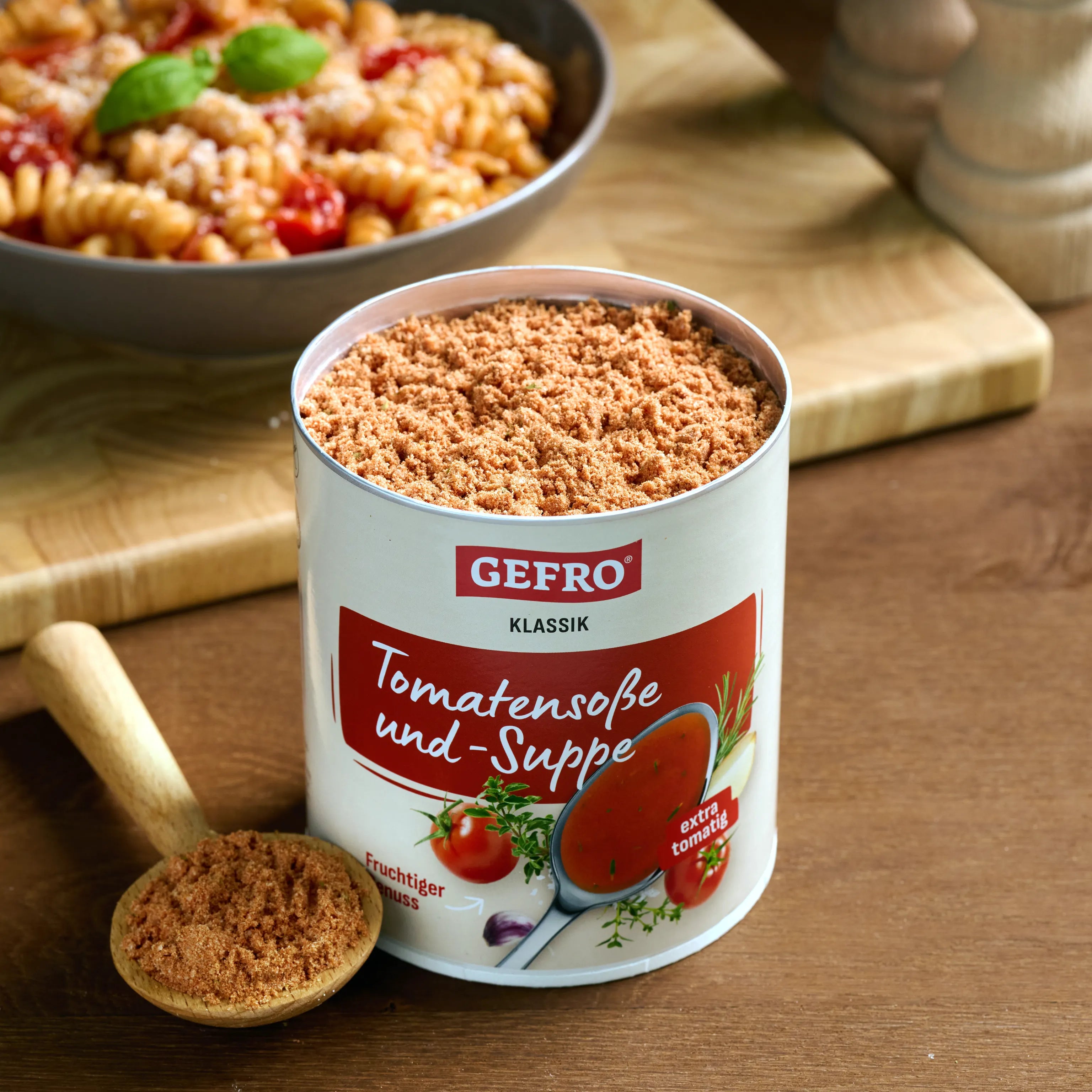 Dose GEFRO Tomatensoße und-Suppe mit Pulver und Holzlöffel, im Hintergrund ein Teller mit Nudelgericht.