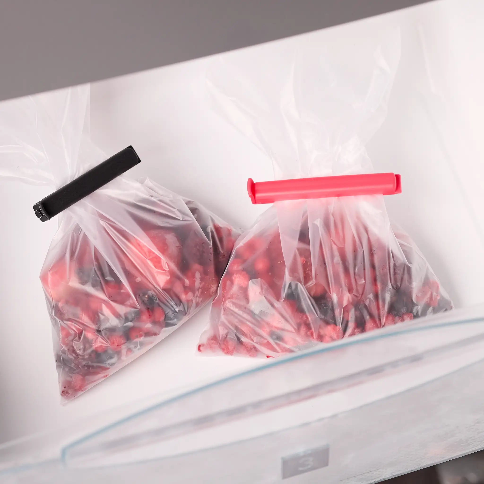 Zwei Gefrierbeutel mit Beeren im Gefrierfach, verschlossen mit wiederverwendbaren Beutelclips in Schwarz und Pink