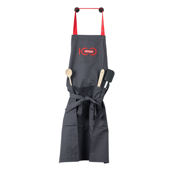 Dunkelgraue Küchenschürze mit roten Trägern, GEFRO-Logo und Fronttaschen mit Kochlöffel und Pfannenwender