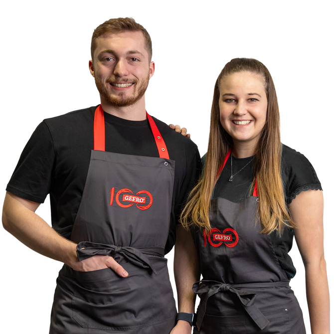 Zwei lächelnde Mitarbeitende in schwarzen Shirts und grauen GEFRO-Schürzen, freundlich und serviceorientiert präsentiert.