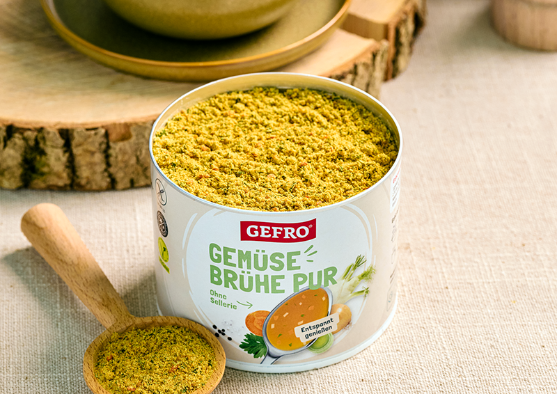 Dose GEFRO Gemüsebrühe Pur mit offenem Brühepulver und Holzlöffel auf hellem Tuch dekorativ präsentiert