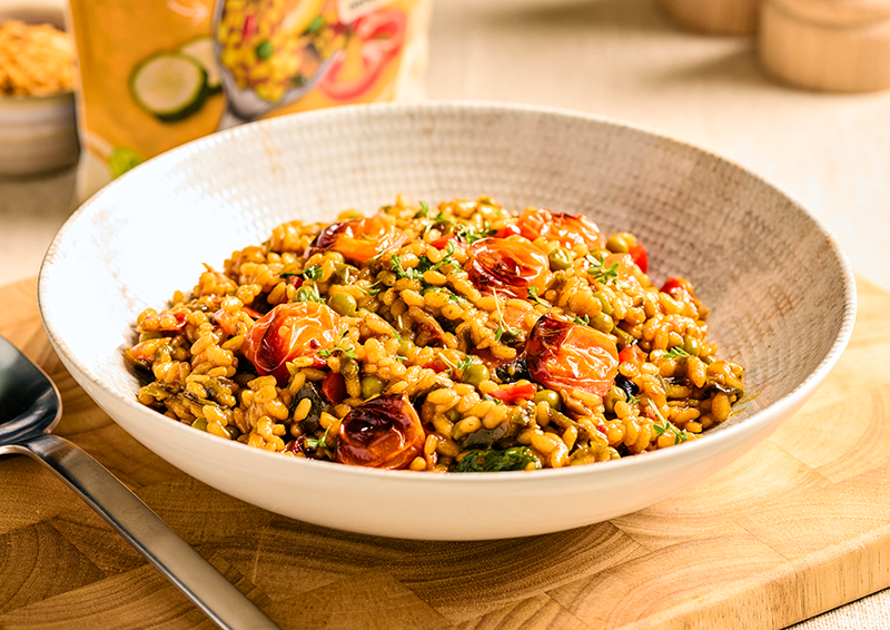 Schüssel mit würziger Reis-Gemüse-Pfanne mit gerösteten Cherrytomaten auf Holzbrett serviert